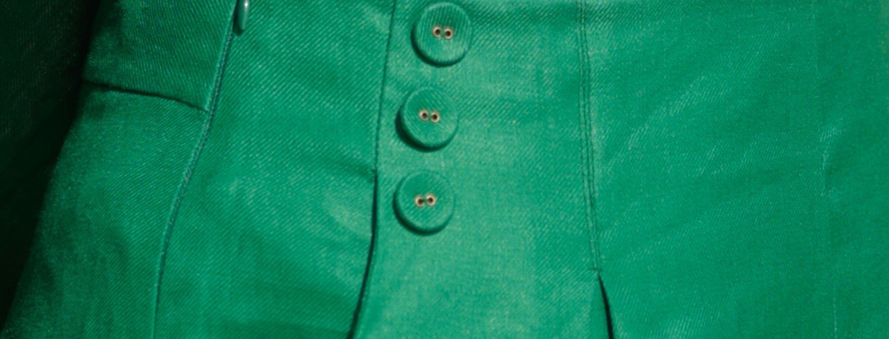 close up the sailor button details of high-waisted, emerald green tailored linen pants for women illustrating the hypoallergenic properties of linen clothing and why linen is good for sensitive skins. 