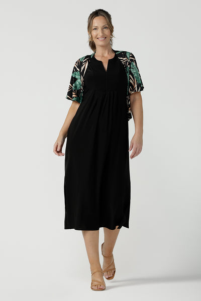 Women's black dress in jersey for women. Pictured on a size 8 for petite to plus size women 8-24. Made in Australia in soft black jersey featuring a v-neckline and pleated front. Styled with a tropical printed shrug. 