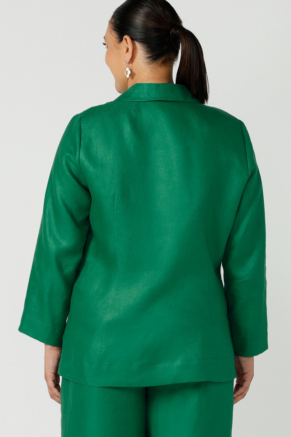 Back view of a size 12 woman wears a soft linen blazer jacket with a tailored design. A transeasonal linen work jacket, in a beautiful emerald green colour. Australian-made using sustainable 100% linen fabric. Size-inclusive fashion 8-24 for corporate casual workwear.
