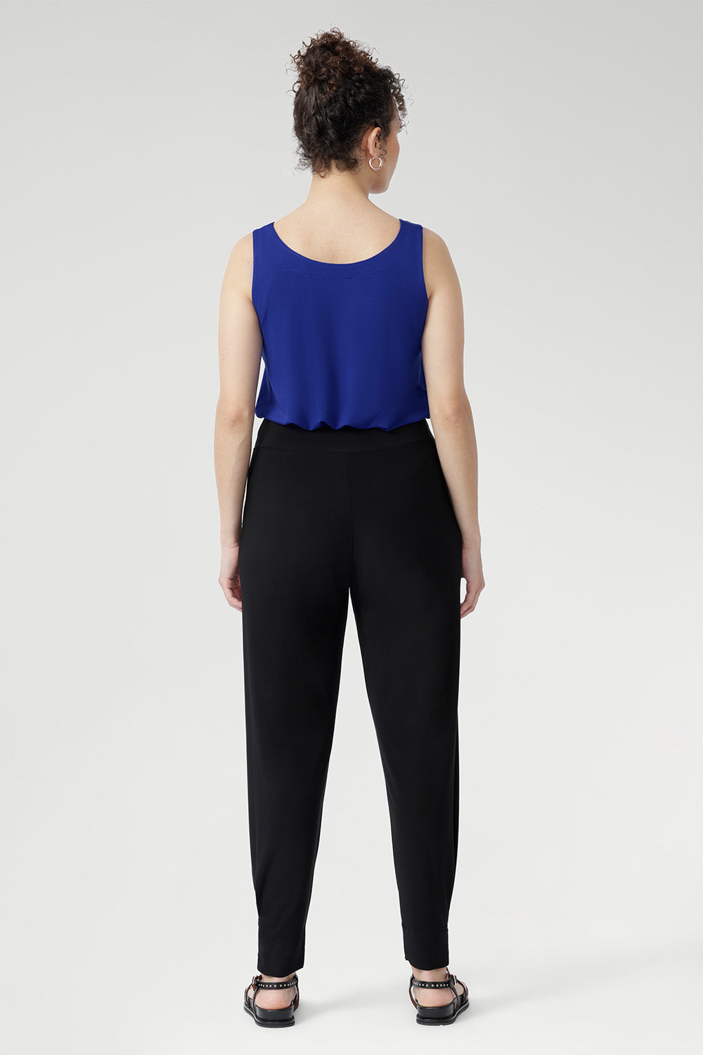 The Indi Pant combines comfort and style in a sleek, tapered silhouette. Made from lightweight black dry-touch jersey with stretch, it features a mid-rise pull-on fit, front gathers, and ankle cuffs with tuck detail. Easy to dress up with a blazer or wear casually for travel days. Available in two heights.