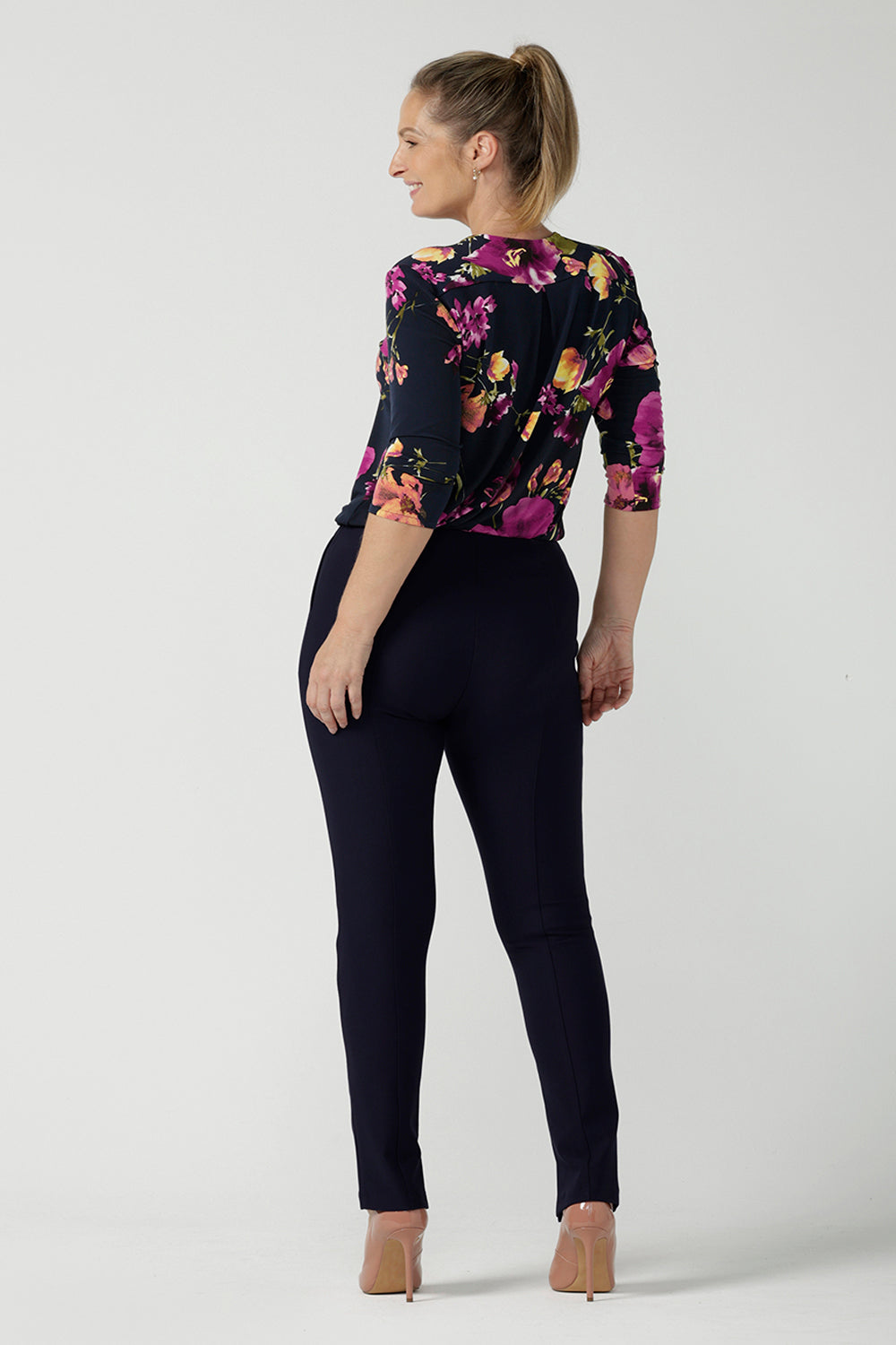 Back view of a size 10 woman wears the Jaime Top in Celeste. A comfortable workwear top that is easy care jersey. Featuring 3/4 sleeves and a v-neckline. Made in Australia and size inclusive. Size 8 - 24. Styled back with the Navy Brooklyn pants.