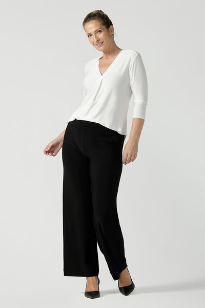 A size 10 woman wears the Jaime top in Vanilla. A comfortable workwear top for women in soft dry touch easy care versey. Featuring a v-neck with pleat front and bind. 3/4 sleeve and made in Australia for women size 8 - 24. Styled back with Black Monroe pants. 
