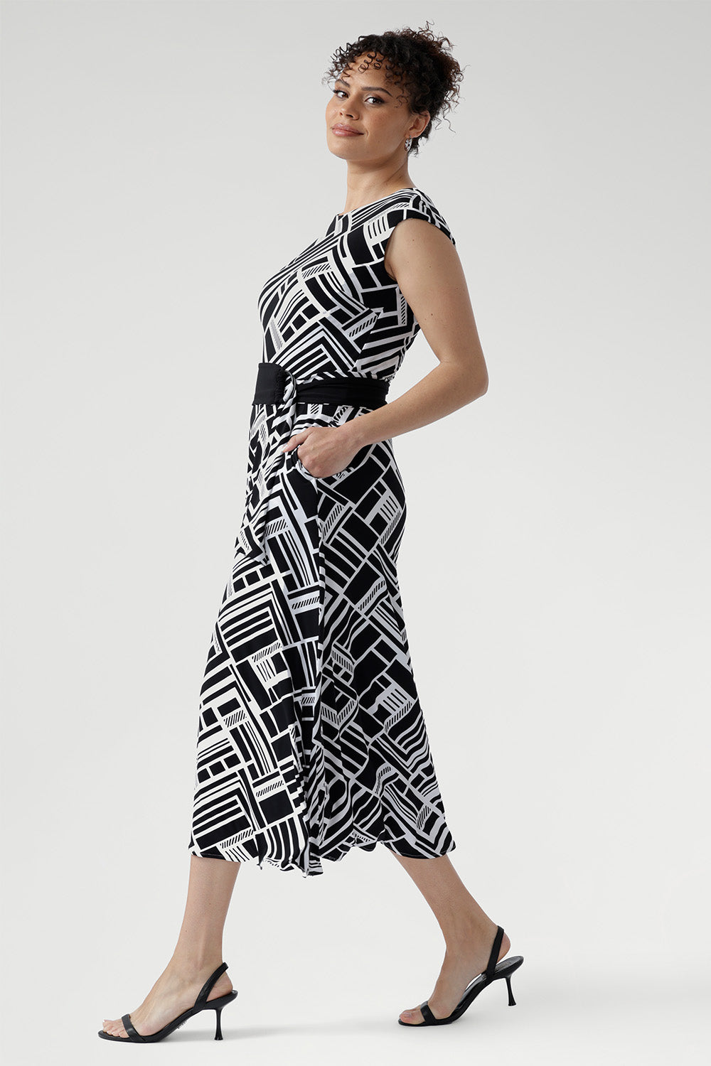 This sleeveless dress is a standout choice for summer days, office wear, or weekend outings, blending timeless style with modern versatility. Size 10 women wears black and white dress with matching belt and kitten heels.
