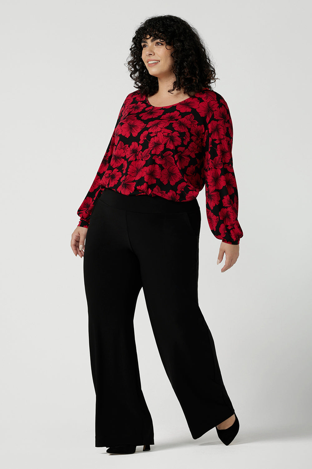 Front view of a size 18 woman wearing the scoop neck bold poppy top with balloon sleeves. Curved hemline and cuffed sleeves. Made in Australia for women size 8 - 24. Styled back with the Monroe pant in black, a straight leg comfortable corporate work pant.