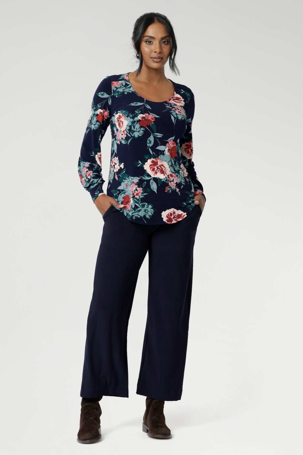 Crafted from a premium dry-touch jersey with soft stretch, the Vintage Rose print blooms across a deep navy base, with floral accents in pink, red, and blue. Designed and made in Australia for women in sizes 8 to 24. Size 10 model wears her blouse untucked over navy work pants.