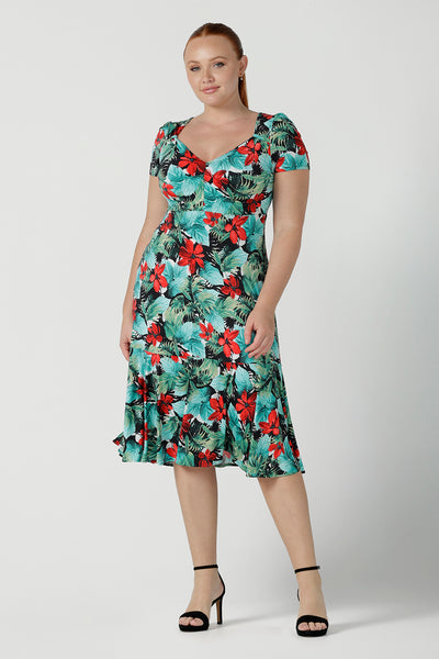 Size 12 woman wears the Jillian dress in Havana. A beautiful tropical print with a green leaf print and red flower on a white base that is tropical inspired. A sweetheart neckline style with an empire line. Tier on hem. Made in Australia for women. Size 8 - 24.
