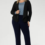 The ideal workwear pant for the combination of comfort, style, and ease. Size 18 woman wears navy workwear pants with blue blouse, black cardigan & silver sneaker.