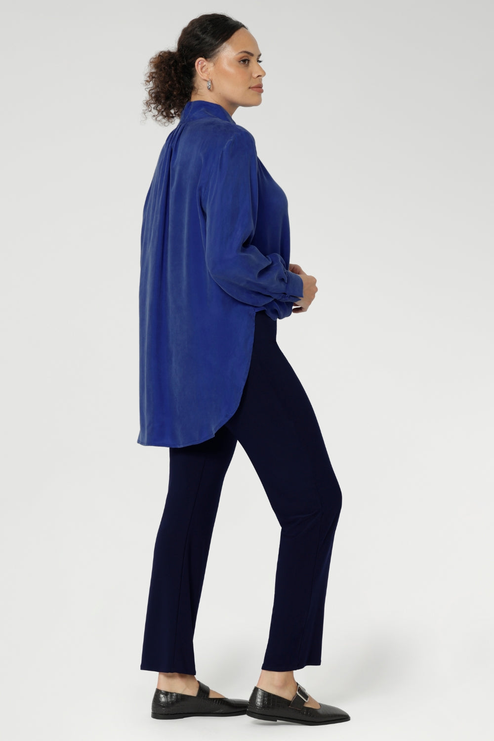 The ideal workwear pant for the combination of comfort, style, and ease. Size 10 woman wears navy workwear pants with long cobalt blouse and brown ballet flats.