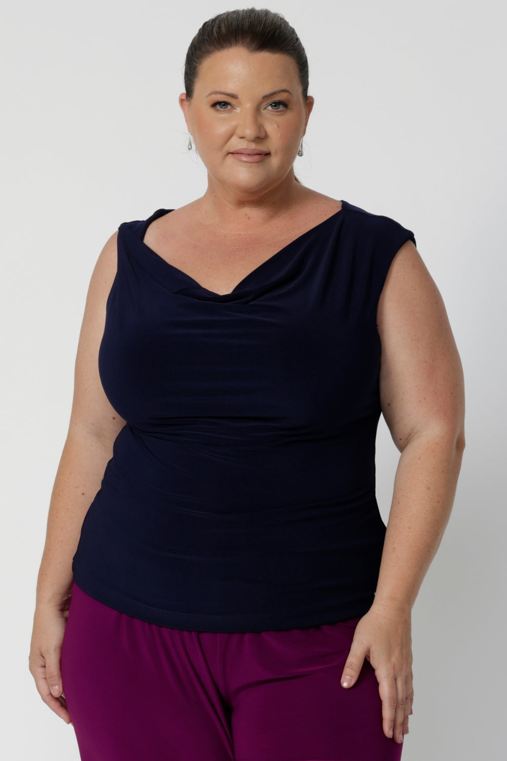 Size 18 woman wears reversible navy top with a cowl neckline and twisted shoulder detail front facing with silver jewellery and bright bold pants. Jordan tops are available in sizes 8-24, for plus & petite size styling.