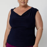 Size 18 woman wears reversible navy top with a cowl neckline and twisted shoulder detail front facing with silver jewellery and bright bold pants. Jordan tops are available in sizes 8-24, for plus & petite size styling.