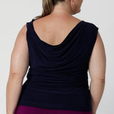 Reversible navy top with a cowl neckline and twisted shoulder detail facing the back for a feminine drape across the back and shoulders. Plus size woman wears her navy workwear top with magenta coloured pants.