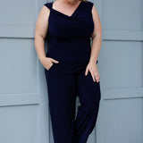 Image features woman over 40 wearing a navy cowl neckline top, paired with matching navy pants for a chic faux jumpsuit effect. The reversible double-layer design allows you to wear it with the cowl neck facing forward, or flip it around to reveal a boat-neck style, offering a more open, structured silhouette. Shop Jordan Tops now in sizes 8-24.