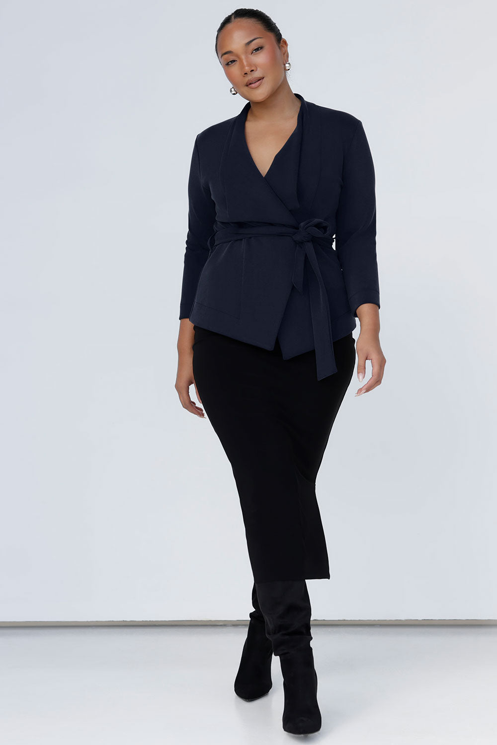 A size 10 woman wears the Lyndon Jacket in Bluestone. A wrap style jacket with waist belt and collared neckline. Made in soft luxurios modal. Rug up on the way to the office or weekend winter get away. Made in Australia for women size 8 -24. Styled back with an Andi skirt in black. 