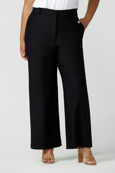 Close up of good full length trousers for plus size women, these Navy blue, tailored wide leg pants are shown on a size 18, curvy woman. Worn with a short sleeve, white bamboo jersey top, these elegant pants wear for work as smart casual wear. Shop made in Australia trousers for women online at women's clothing brand Leina & Fleur.