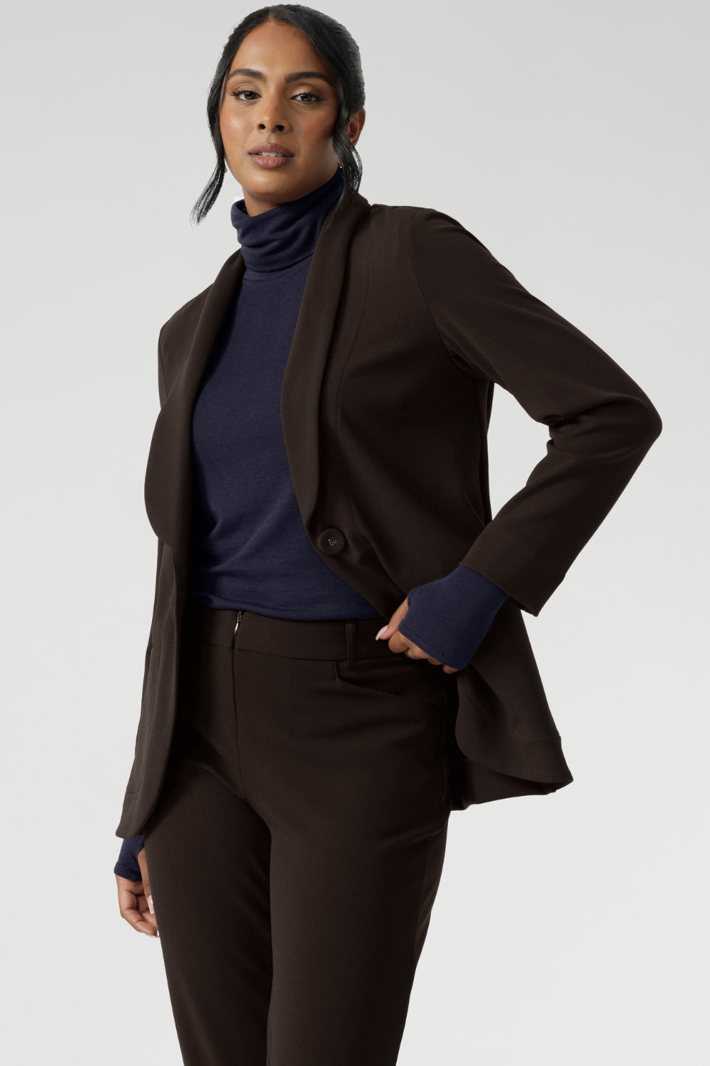 Size 10 model wears navy long-sleeved top featuring high turtleneck for added comfort and warmth. Crafted from lightweight, warm tencel wool fabric. Model pairs her wool top with brown suiting for an elevated back to work outfit.