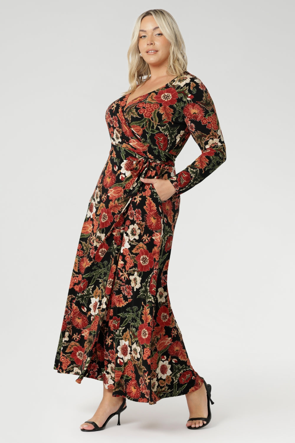 Size 18 woman wears elegant full-length wrap dress features long sleeves, a flattering V-neckline, and practical side pockets, combining chic design with everyday functionality. Made from a soft-stretch jersey fabric and available in sizes 8-24.