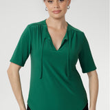 The Kodi Top is expertly crafted from our signature dry-touch stretch jersey, combining luxe tailoring with all-day comfort. Size 10 woman wears her elbow length top paired with black work pants.