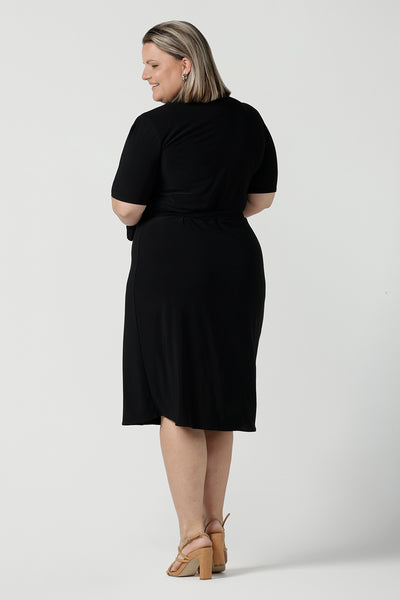 Back view of a size 18 woman wears the Kriss dress in black. A functioning wrap work dress in soft black jersey. Great for being comfortable in the office. Made in Australia for women size inclusive fashion 8 - 24.
