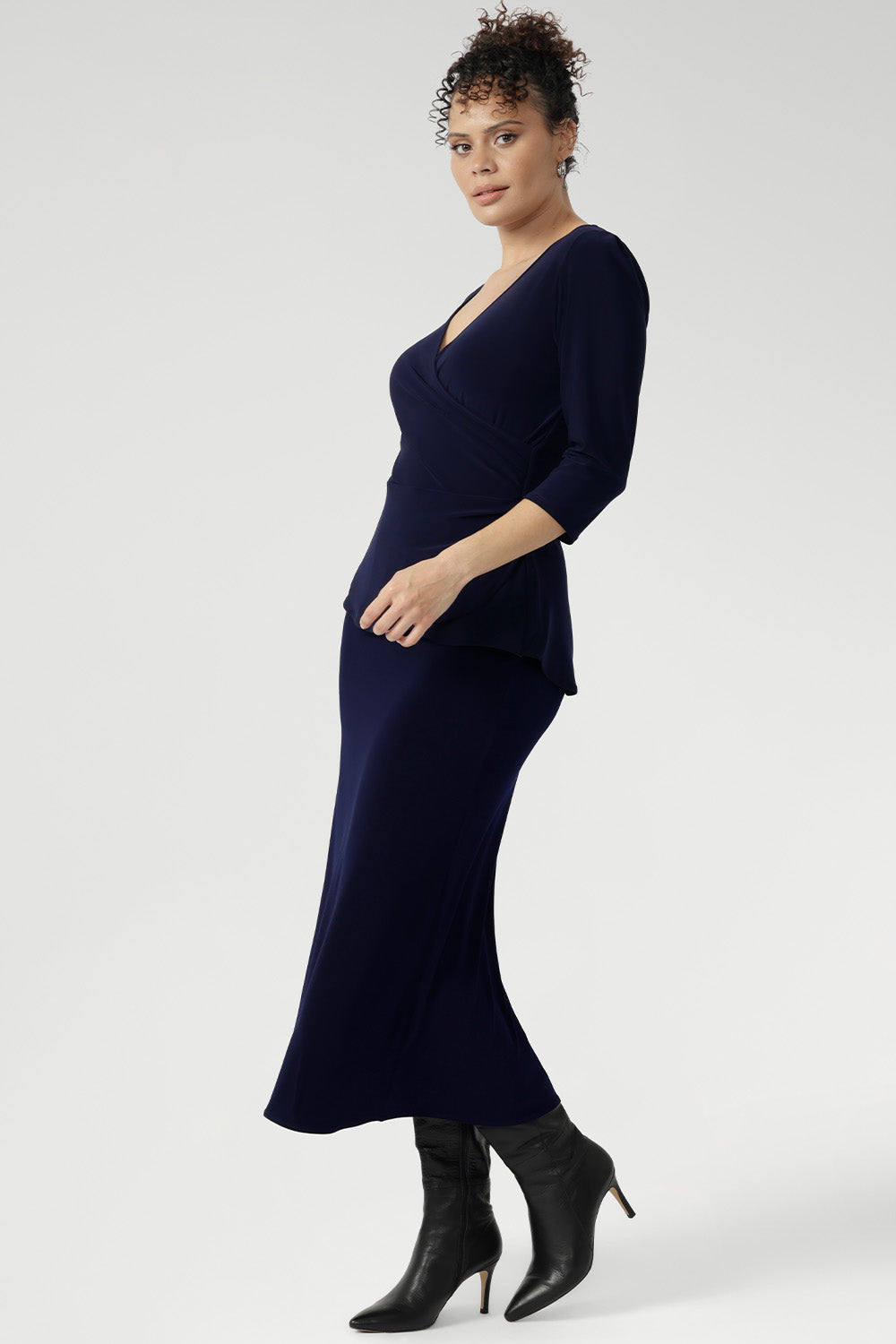 Whether you're in the office or heading to after-work events, the Kyle Top delivers confidence and style with ease. Size 10 model wears navy wrap top with navy midi skirt and black boots for a faux dress look.