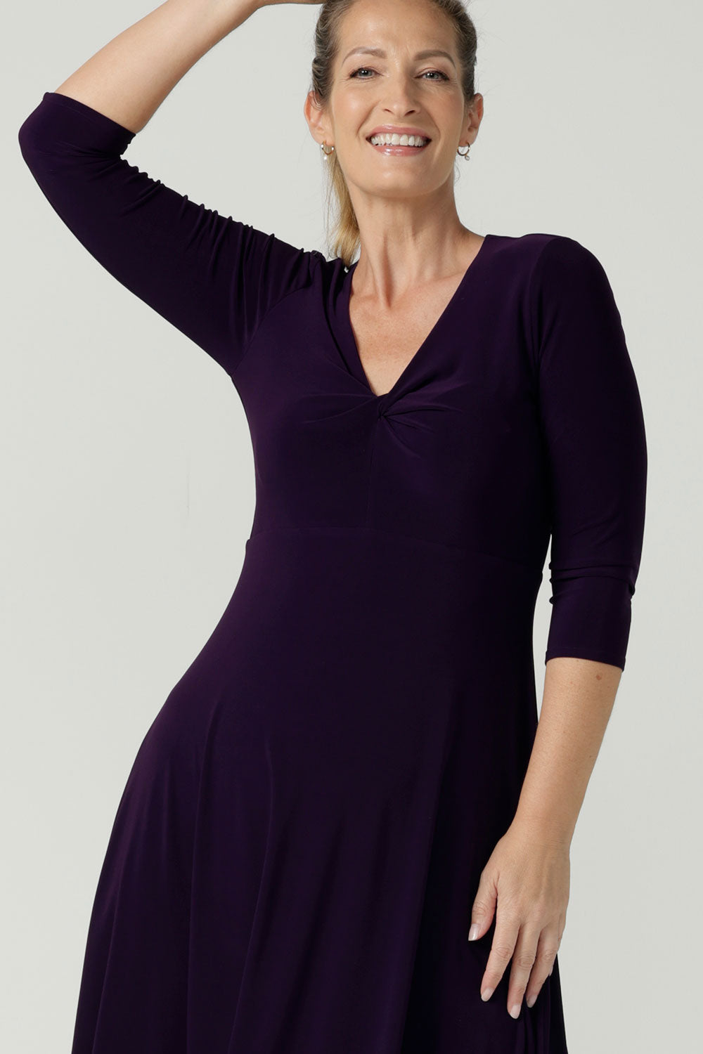 Close up of a size 10 Woman wears the Amethyst Kyra dress in jersey. Made in Australia for women. Beautiful twist front neckline with 3/4 sleeve, high-low hem, empire line. Work wear for women and easy care. Great wedding guest outfit, mother of the bride. Made in Australia for women size 8 - 24.