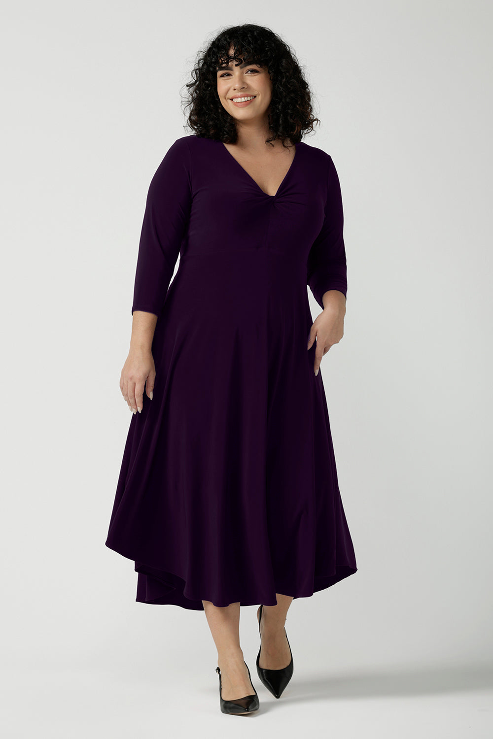Size 18 Woman wears the Amethyst Kyra dress in jersey. Made in Australia for women. Beautiful twist front neckline with 3/4 sleeve, high-low hem, empire line. Work wear for women and easy care. Great wedding guest outfit, mother of the bride. Made in Australia for women size 8 - 24.