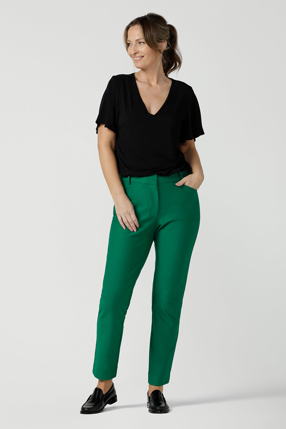 A flutter sleeve, black top for work and casual wear, this tailored top is worn by a size 10, 40 plus woman. Worn with tapered leg, green tailored pants for work, both are made in Australia. Shop women's black tops online at Australian and New Zealand women's clothing brand, Leina & Fleur.