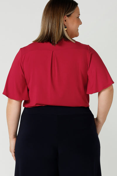 Back view of a Happy curvy woman wears the Lila Top in Flame bamboo in a Christmas red colour. The bamboo material is breathable, soft and temperature regulating. The Lila top features a flutter sleeve and deep v-neckline. Made in Australia for women size 8-24.
