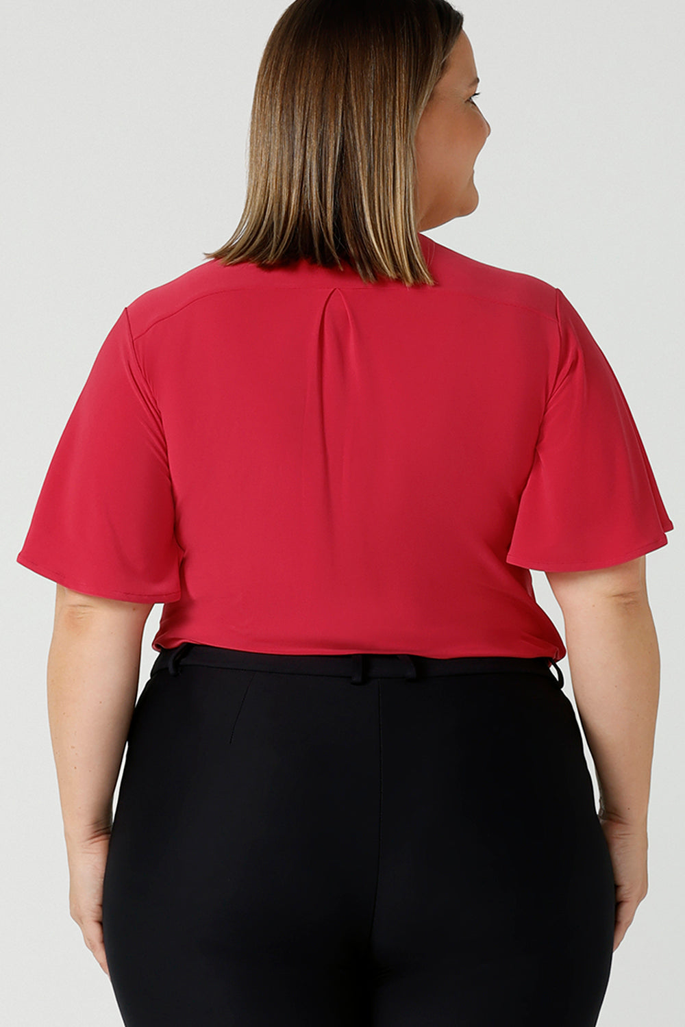 Back view of a curvy woman wears Lila flutter sleeve top with v-neckline. A comfortable statement piece from the office to the weekend. Designed and made in Australia for women size 8 - 24.
