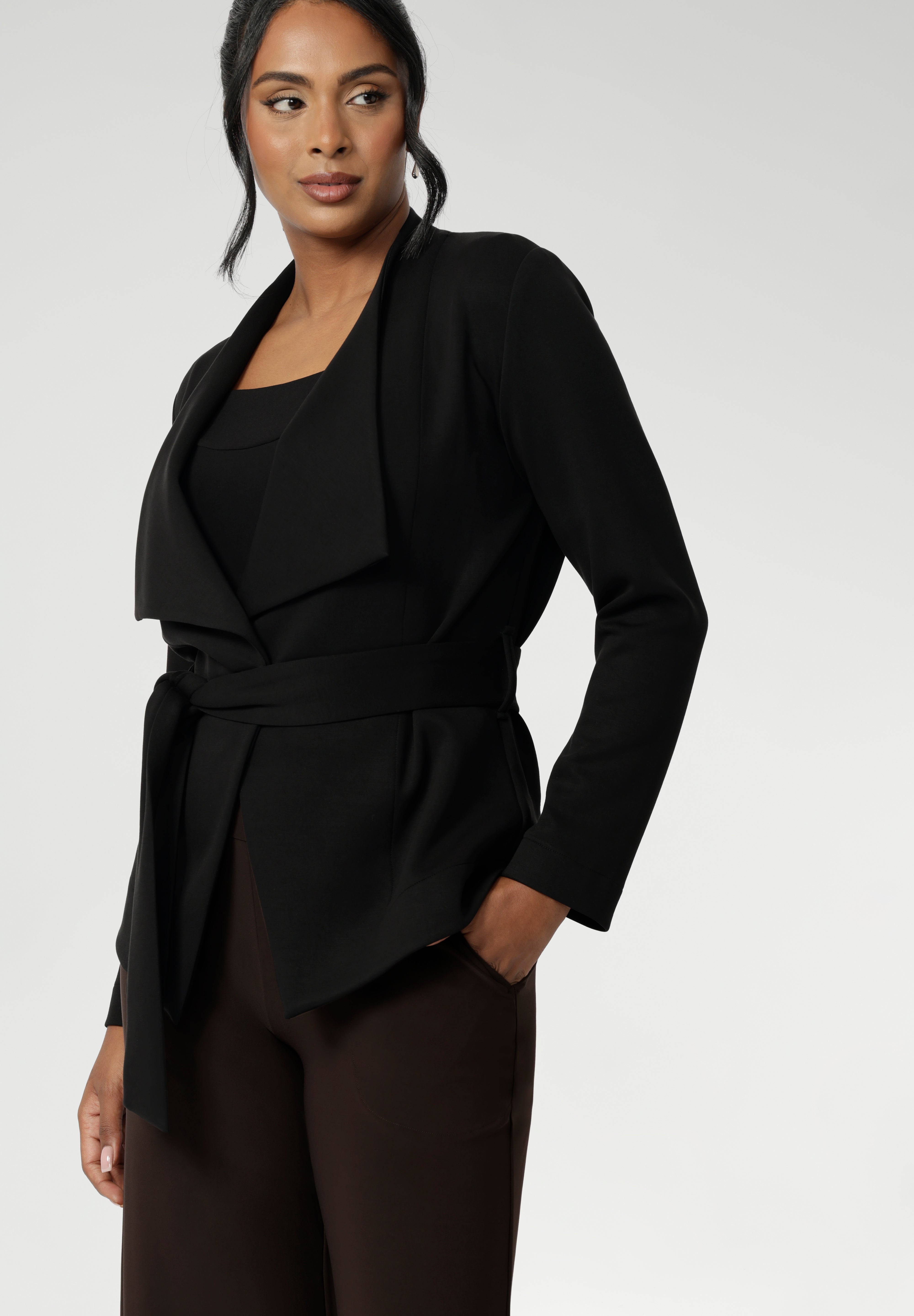 The Lyndon Jacket in Black features a stylish double-layer design with angled front panels for a sleek, modern look. It comes with a detachable waist tie and belt loops, so you can wear it open or cinched to flatter your silhouette.