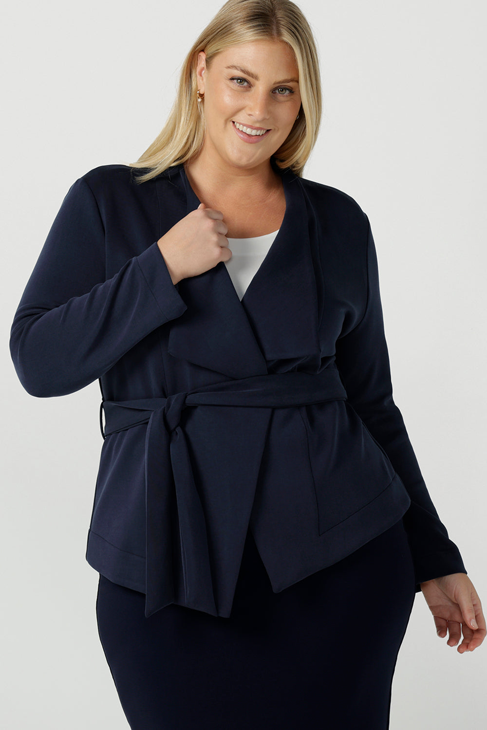 A size 18 woman wears the Lyndon Jacket in Bluestone. A wrap style jacket with waist belt and collared neckline. Made in soft luxurios modal. Rug up on the way to the office or weekend winter get away. Made in Australia for women size 8 -24. 