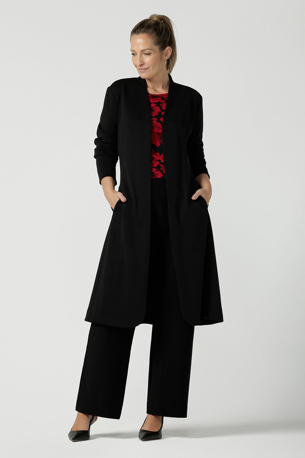 Size 10 woman wears the Mason top in Bold Poppy . A long sleeve jersey top for women with red floral on a black base. Comfortable work top for women size 8 - 24. Soft jersey fabric and made in Australia for women. Styled back with the Monroe pant in black a straight leg pant. Styled back with the Sorel Trench in black modal. 
