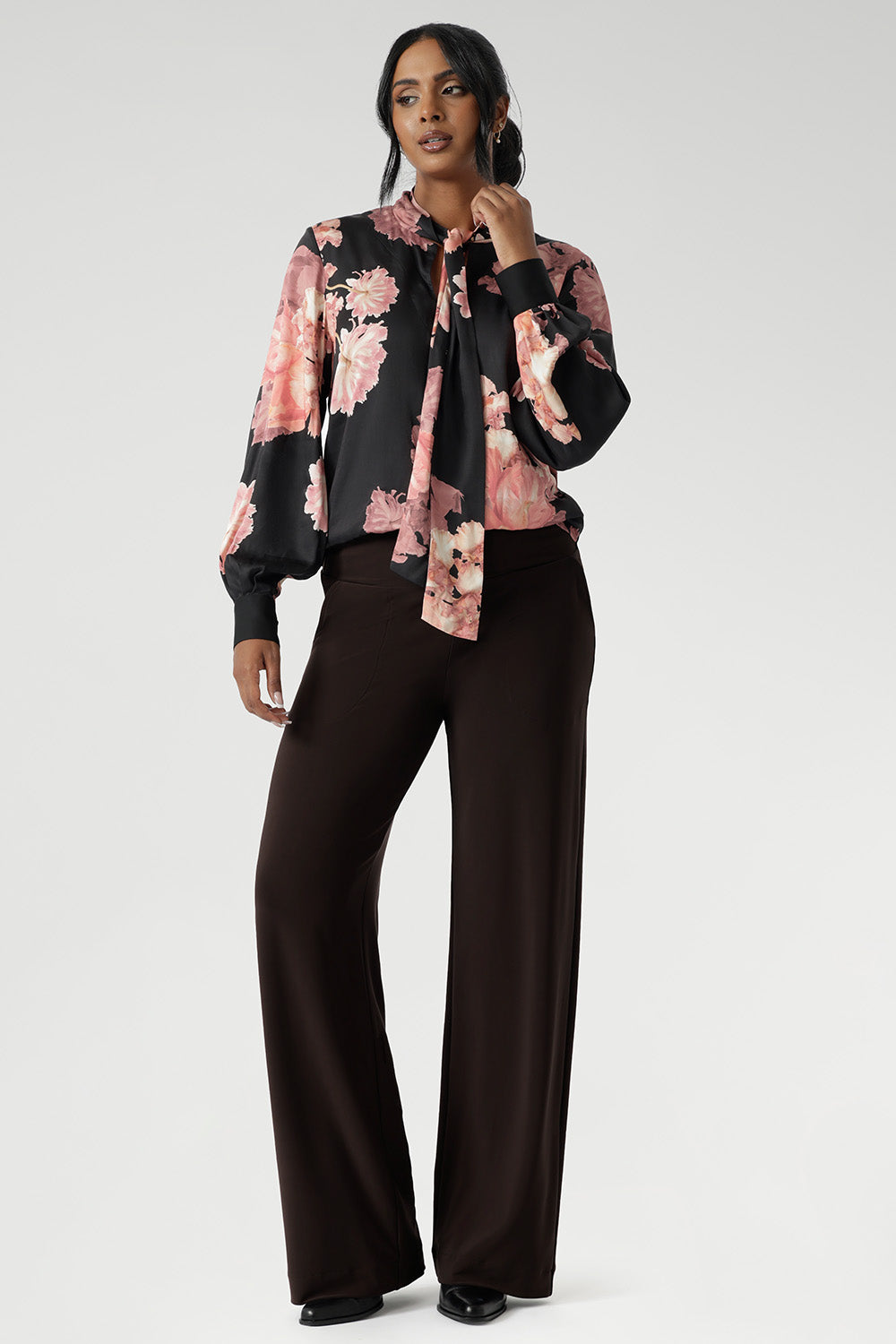 While the fabric offers no stretch, its fluid drape ensures a flattering, comfortable fit. Ideal for pairing with tailored separates or dressed down with denim, the Matisse Shirt brings timeless romance to your wardrobe. Plus size woman wears floral blouse tucked into her straight leg pants.