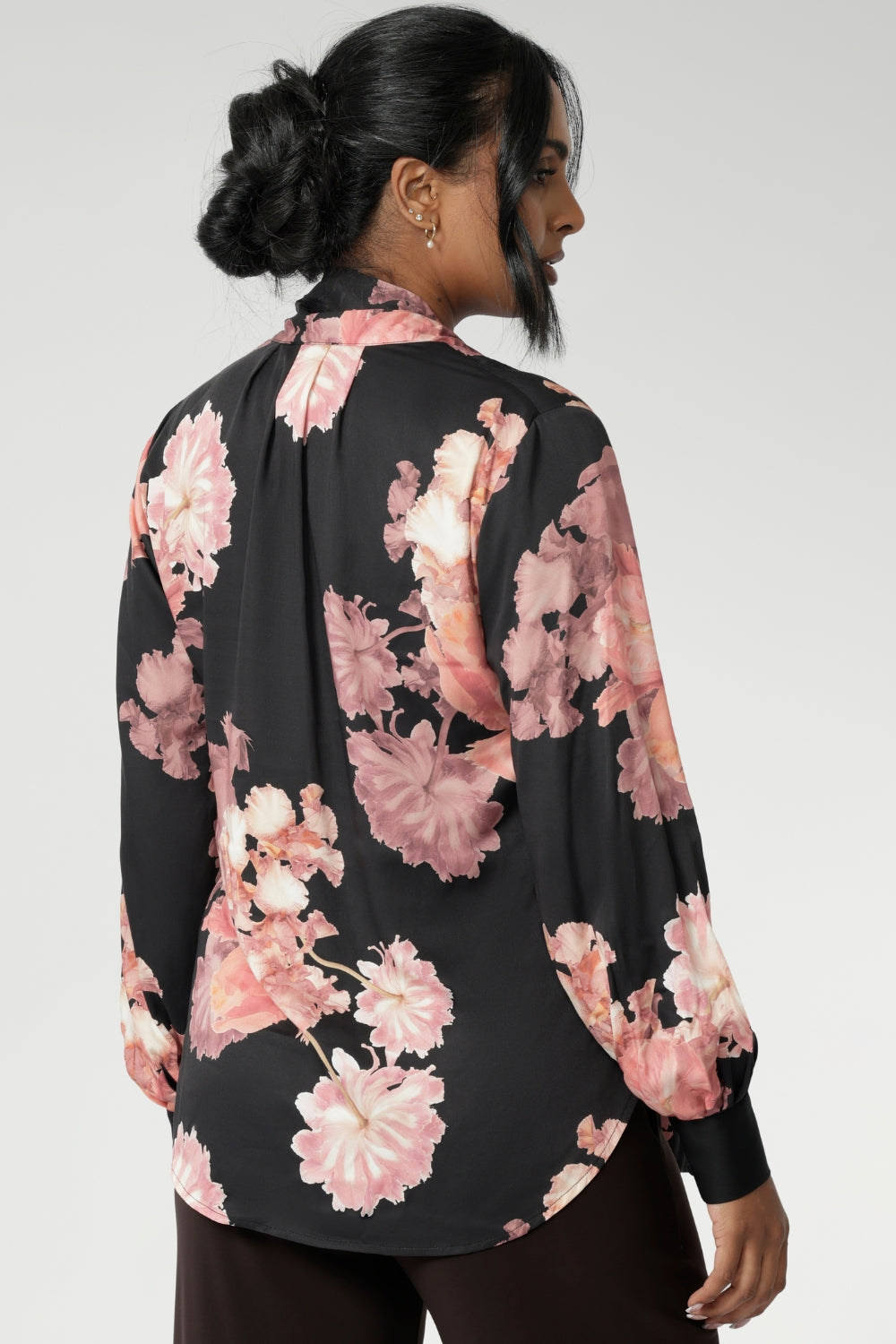 Crafted from a soft, fluid satin rayon fabric, this semi-fitted shirt features a pull-on design with a graceful V-neckline and extended neck ties that can be styled in multiple ways. The romantic floral print blooms across a black satin base, with delicate pink tones adding depth and softness to the look.