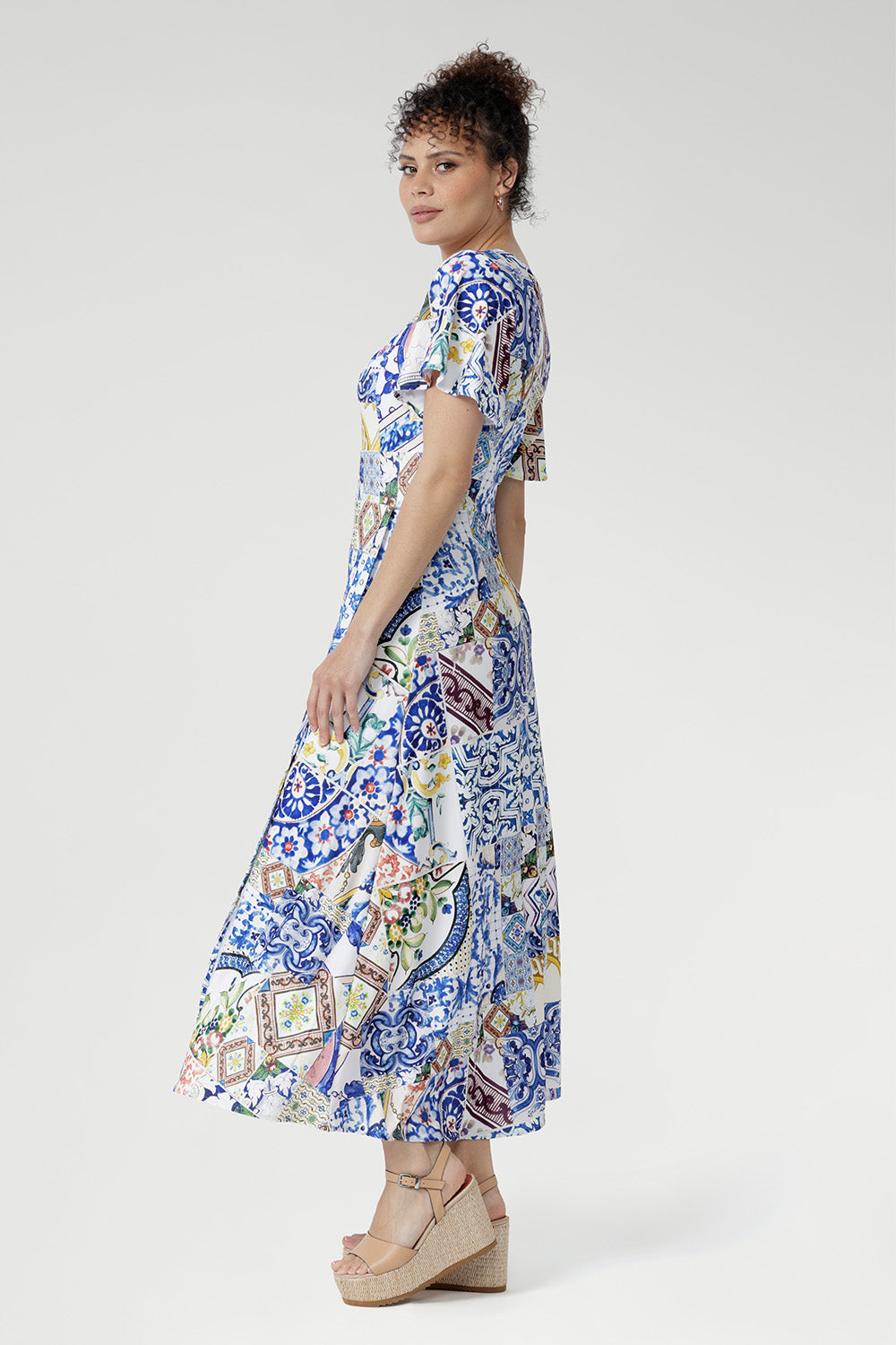 The empire waistline and twist-front V-neck create a naturally flattering shape, while flutter sleeves and a double-layered bodice provide elegant structure and ease. A flowing skirt with an overlap slit adds graceful movement and a touch of allure—perfect for weddings, garden parties, and special celebrations.