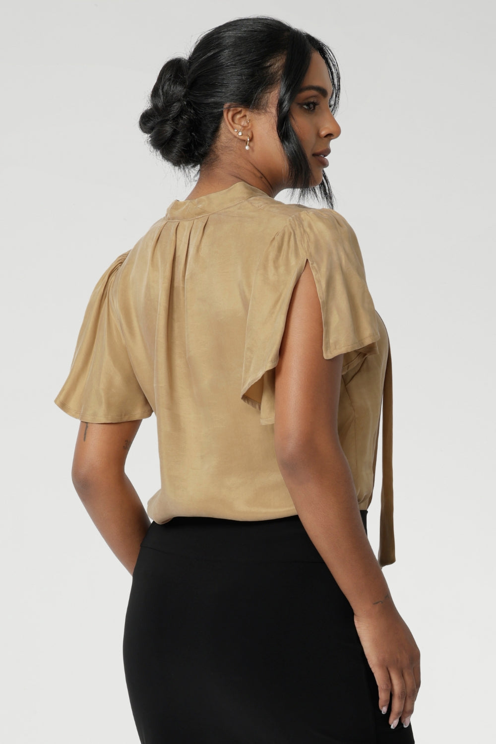 Woven blouse made from luxurious gold soft suede-touch Tencel fabric. This images features a blouse draped beautifully on the body, catching the light in the most flattering way. Though the fabric has no stretch, it offers an effortlessly graceful silhouette that moves with you, creating a striking and sophisticated look. Available in size 8-24.