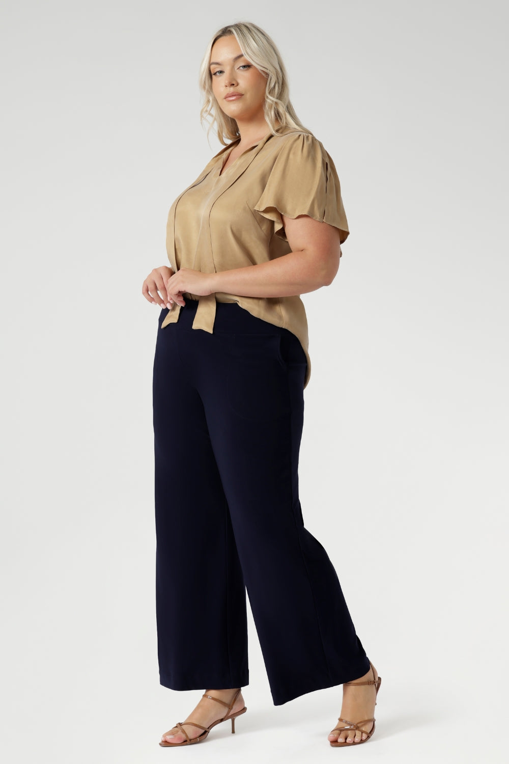 Plus size woman wears semi-fitted design of the Michael Shirt. Tailored yet relaxed feel, this blouse has the right amount of structure without feeling too tight. The V-neckline with delicate neckties adds a touch of feminine elegance, while allowing you to adjust the fit for added comfort and style. The short flutter sleeves, with slits on the shoulders, add a modern, airy feel to the blouse, perfect for this time of year. Available in sizes 8-24.