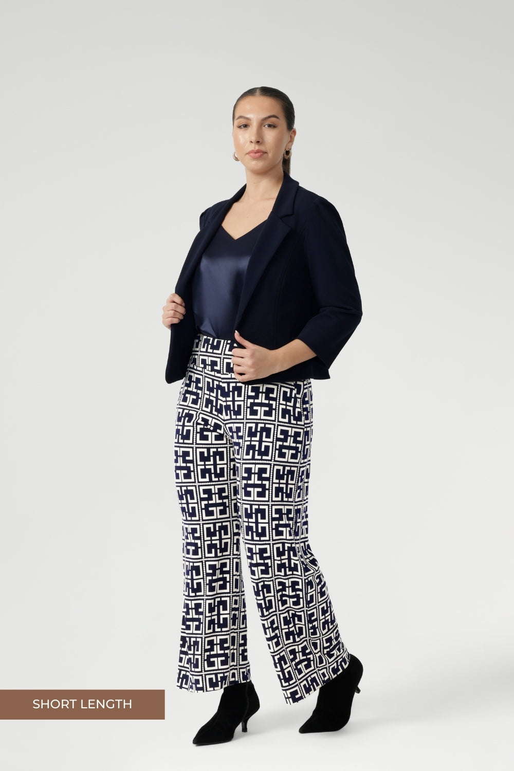 The Monroe Pant features a pull-on waistband that sits smoothly on the body, deep side pockets with topstitching for a tailored touch, and a classic straight-leg cut that transitions seamlessly from workwear to weekend. Size 10 woman wears petite height friendly pants with satin cami and navy jacket.