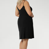 A size 18 woman wears a mini-length, reversible slip in black jersey fabric. The slip has thin straps and is worn with a V neck to the front. Made in Australia to layer under dresses and separates. Plus size slip dress for women. Available in size 8-24.