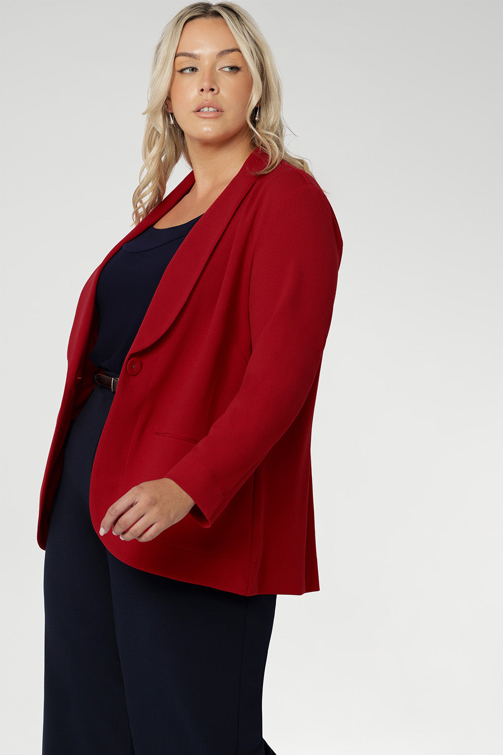 Plus size woman wears the Merit Blazer in Flame, a textured scuba crepe blazer with button front. This red work blazer is worn with red workwear pants and red cami top. Curved hemline and front pockets. Made in Australia for women size 8 - 24.