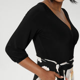 Close up image of Nerida Dress in Blushing Bloom. Black bodice dress has cuffed 3/4 sleeves, and floral skirting. Woman's jersey dress features d ring belt that is printed on one side and black on the other.