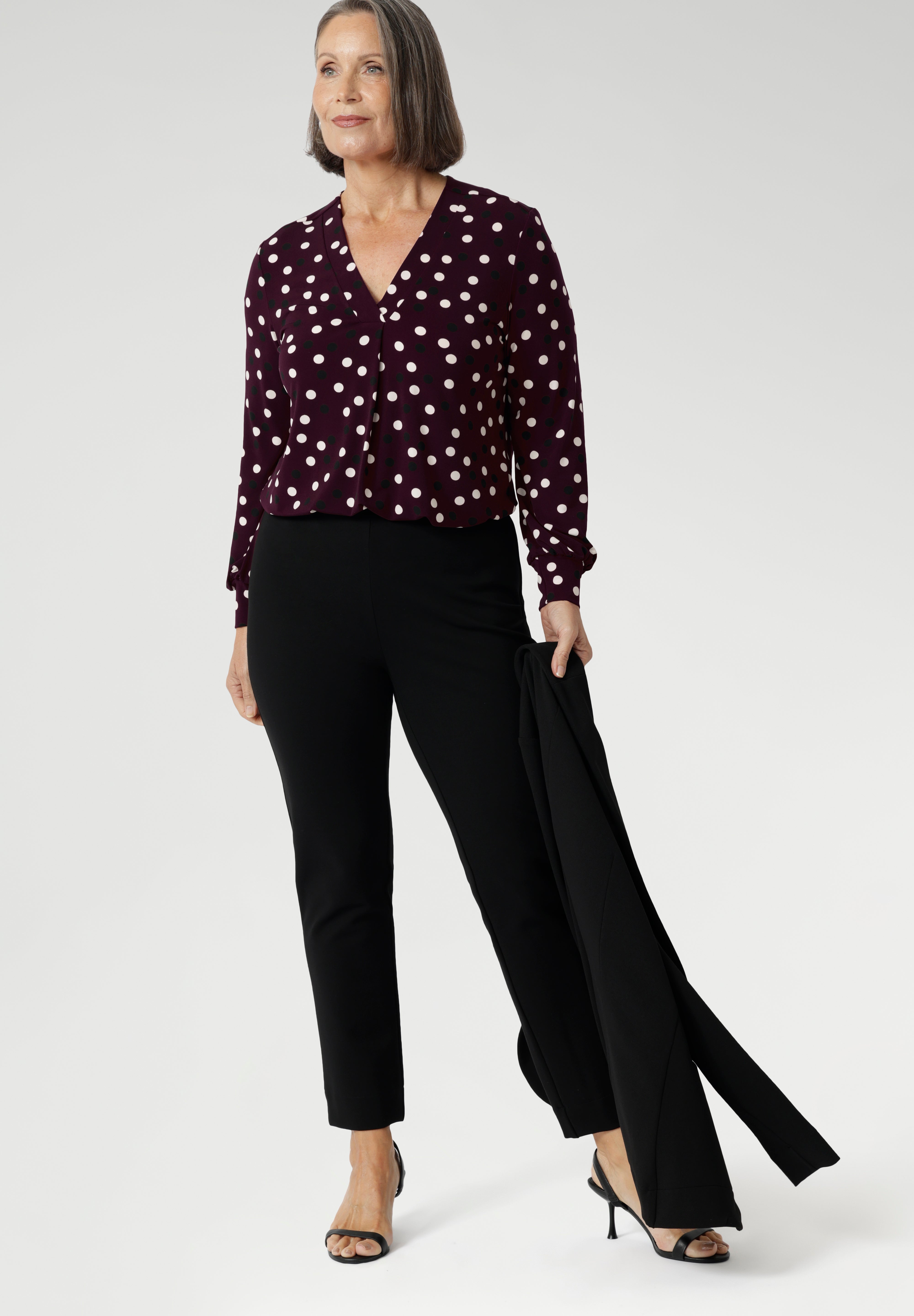 Whether you’re dressing for the office or a day out, the Paeton Top delivers effortless style, comfort, and modern femininity. The Paeton Top in burgundy spot is a standout piece in our luxe separates collection, combining everyday comfort with elevated design. Mature model wears her Paeton Top with black tapered leg pants and matching black work wear jacket.