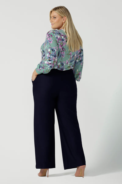 Back view a size 18 woman wears the Kade tailored pant in Navy. Made in Australia for women size 8 - 24. Styled back with the Paeton top in day bloom. V-necline with pleat front and bind. Made in Australia for women size 8 - 24.