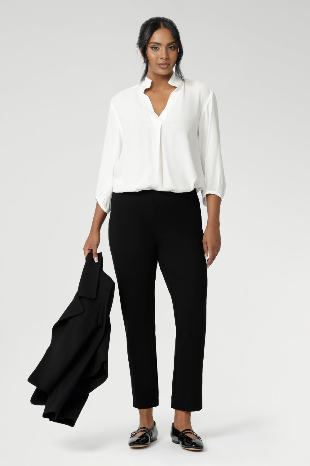A size 10 woman wears the Paxton Pant in black. A loose fitting ponte pant in black. A slack pant with cropped length. Made in Australia for women size 8-24. Styled back with the Arley Top in white.