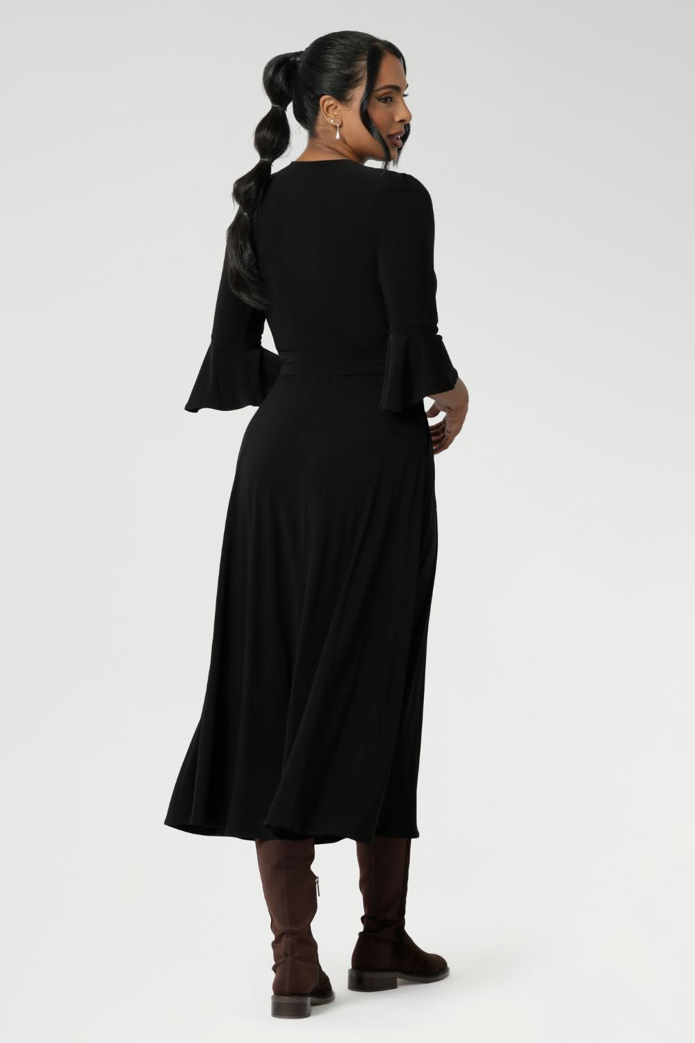 Back view of a size 10 corporate woman wears the Portia dress in Black. A wrap dress in black with tie side and 3/4 sleeve. Styled with long brown boots. Made in Australia for women size 8 - 24.