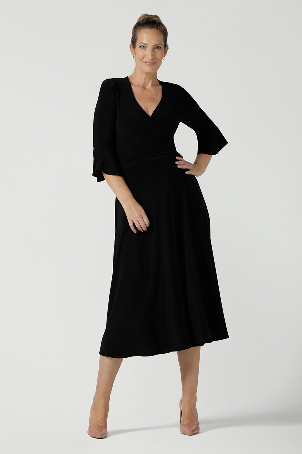 Size 10 corporate woman wears the Portia dress in Black. A wrap dress in black with tie side and 3/4 sleeve. Styled back with pink heels and v-neckline. Made in Australia for women size 8 - 24.