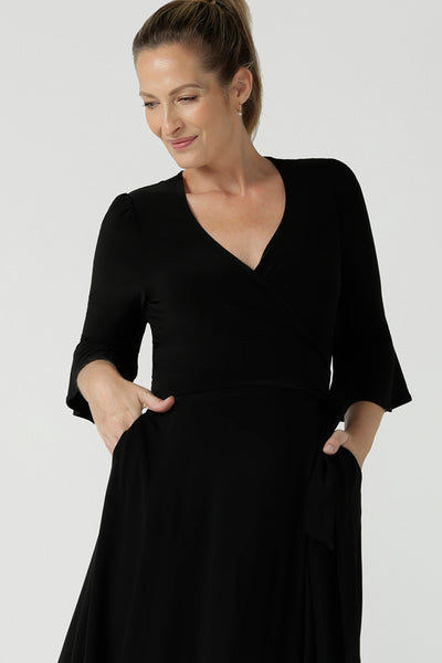 Close up of size 10 corporate woman wears the Portia dress in Black. A wrap dress in black with tie side and 3/4 sleeve. Styled back with pink heels and v-neckline. Made in Australia for women size 8 - 24.