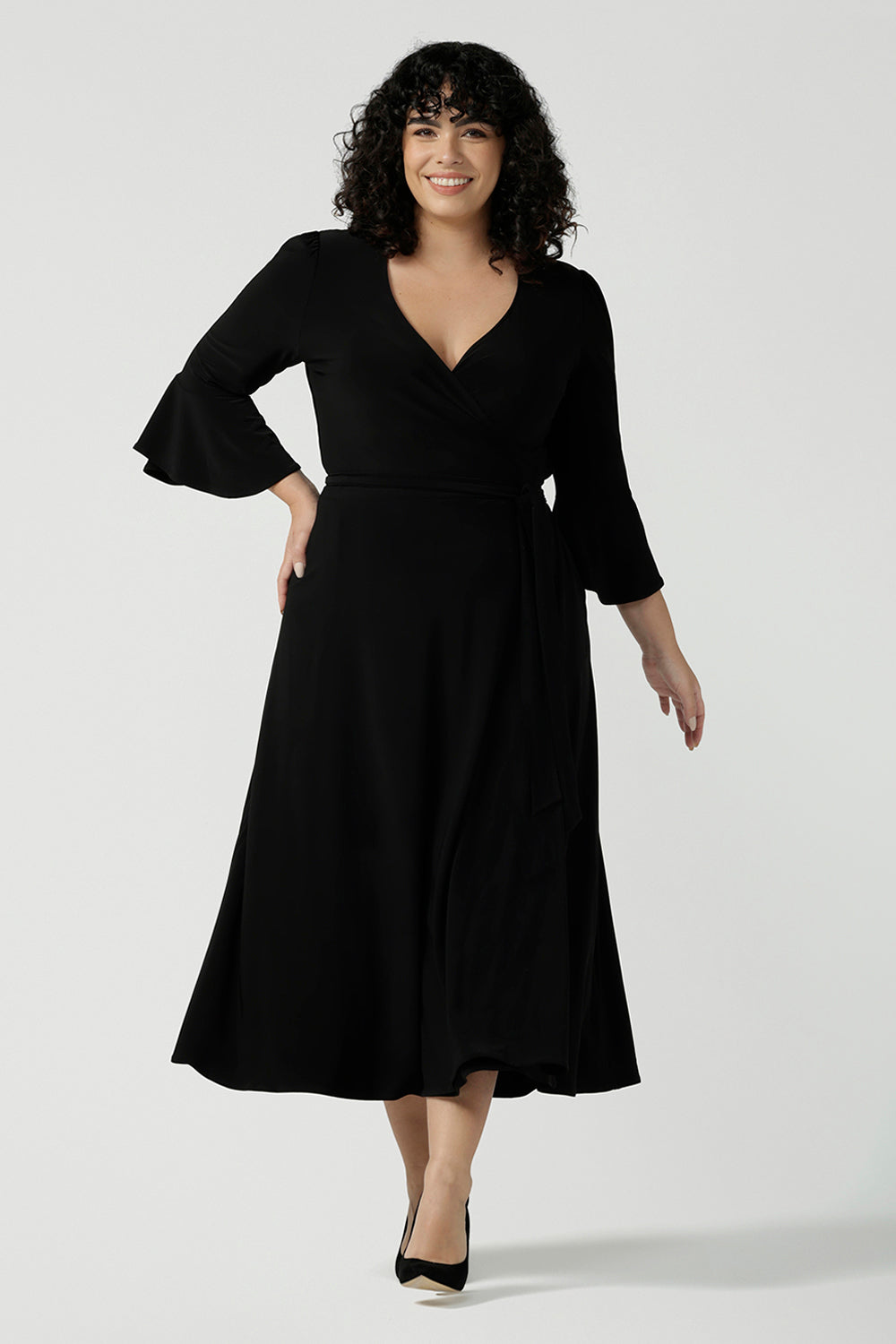 Size 18 corporate woman wears the Portia dress in Black. A wrap dress in black with tie side and 3/4 sleeve. Styled back with pink heels and v-neckline. Made in Australia for women size 8 - 24.