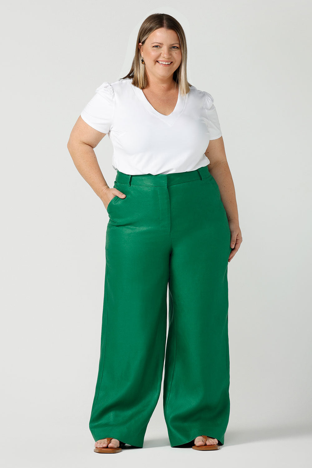 A size 18 curvy woman wears a tailored linen pant in 100% linen. Breathable linen fabrication in a beautiful emerald green colour. The perfect workwear pants with pockets that make great summer pants. Size inclusive fashion designed and made in Australia size 8 - 24. 
