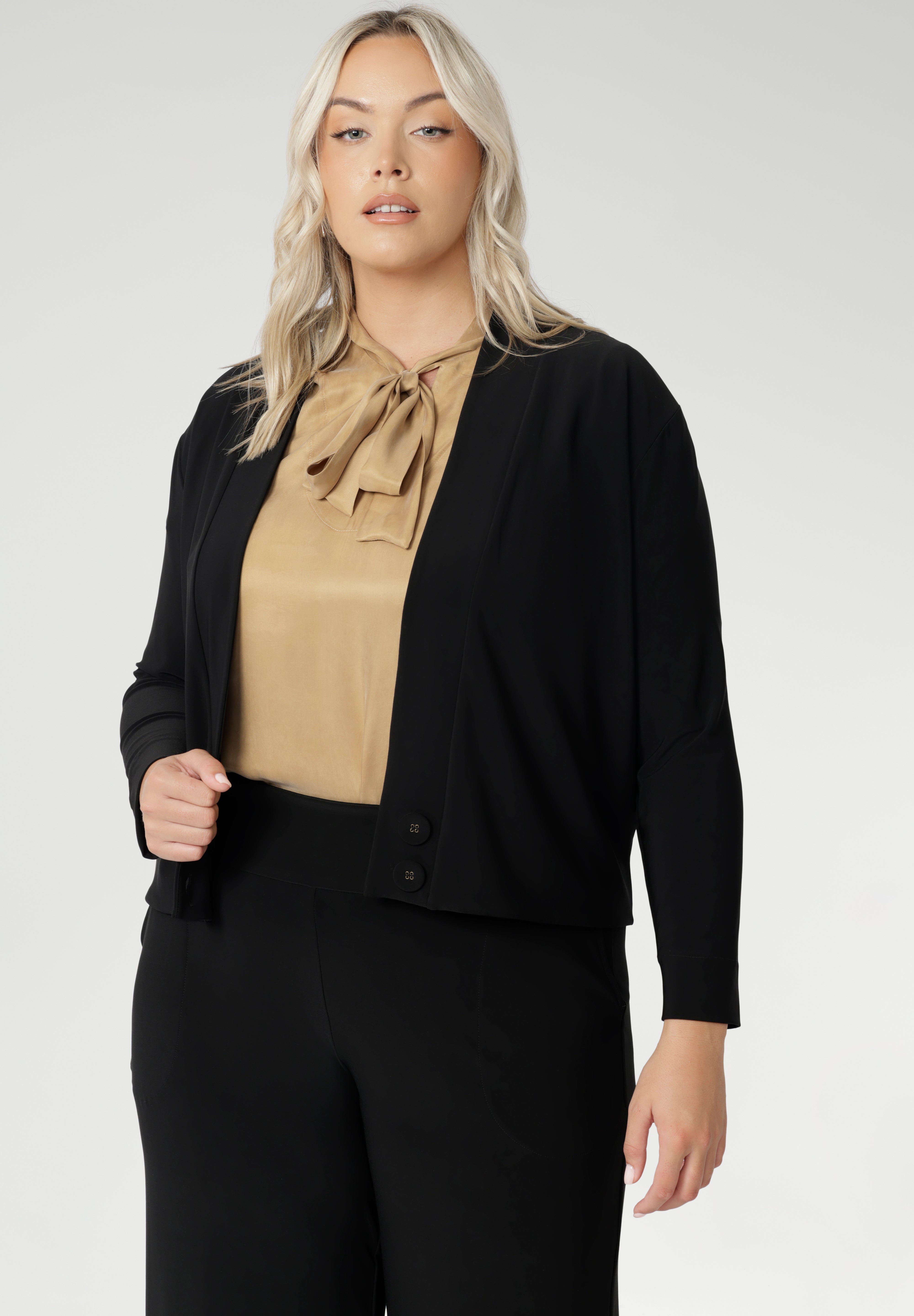 Size 18 woman wears black Jacardi, which is part jacket, part cardigan. This soft touch jacket is a transeasonal cover up. Featuring V-neckline, long sleeves and front buttons. This casual black jacket is made from stretchy and comfortable jersey fabric. Easy care workwear jacket available in sizes 8-24.