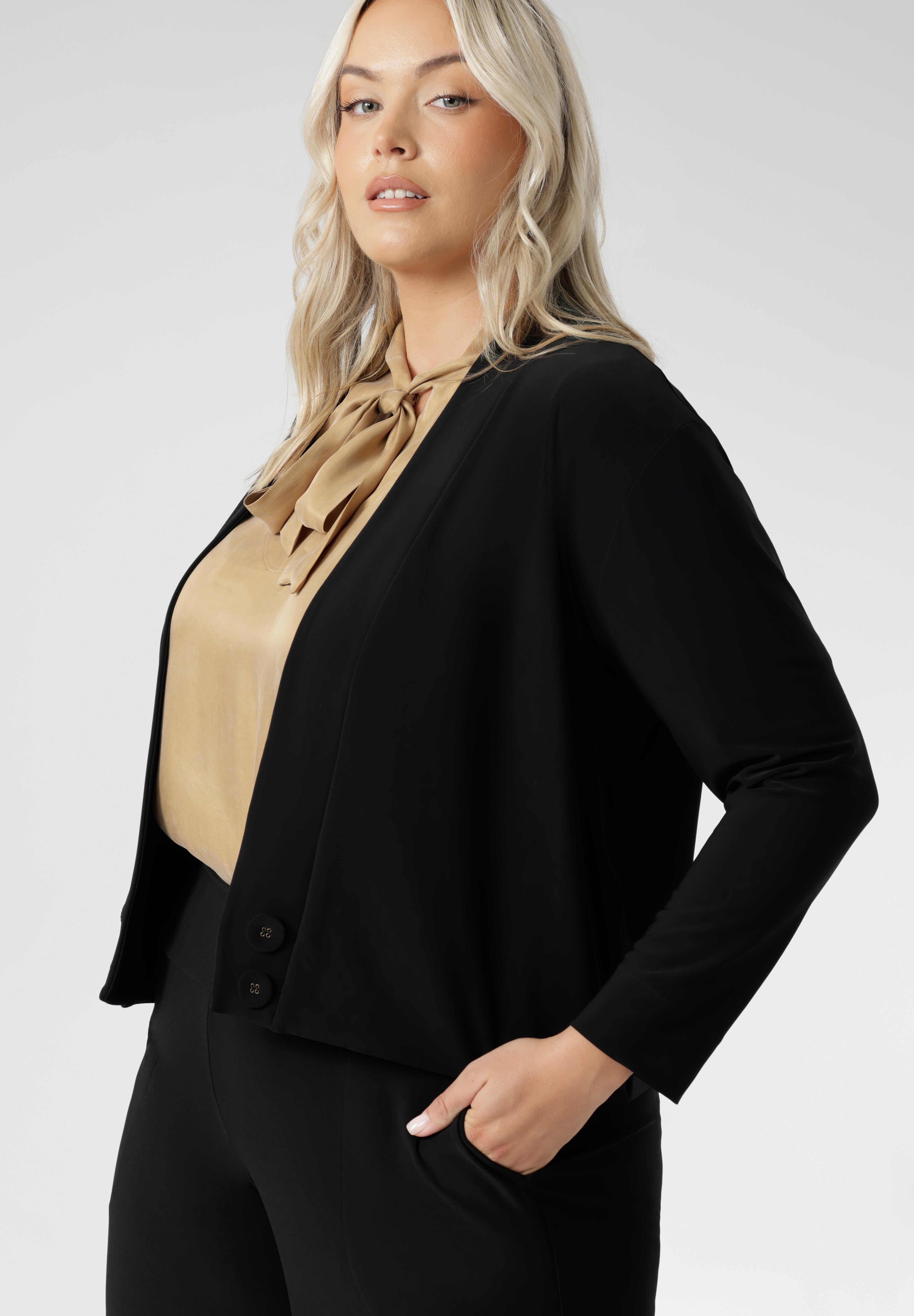 Size 18 woman wears black Jacardi, which is part jacket, part cardigan. This soft touch jacket is a transeasonal cover up. Featuring V-neckline, long sleeves and front buttons. This casual black jacket is made from stretchy and comfortable jersey fabric. Easy care workwear jacket available in sizes 8-24.